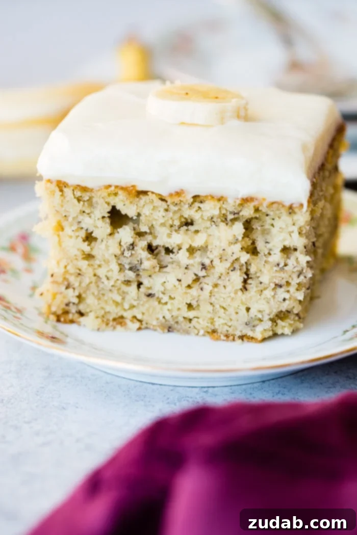 Perfectly Moist Banana Cake 3 A close-up of a perfectly moist slice of banana cake, topped with a generous swirl of creamy, rich cream cheese frosting.