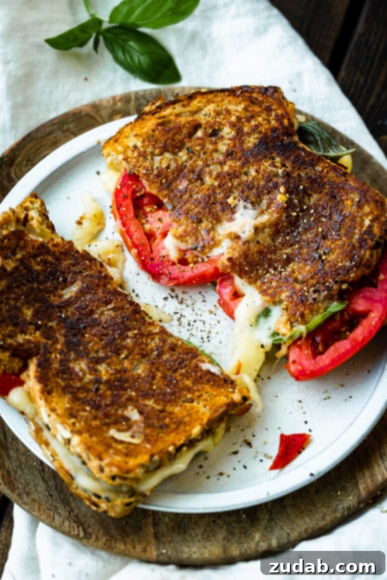 Gourmet Havarti Tomato Basil Grilled Cheese 3 A close-up photo of a Havarti tomato basil grilled cheese sandwich, perfectly sliced in half to reveal the gooey melted cheese, vibrant red tomatoes, and fresh green basil, served on a pristine white plate.