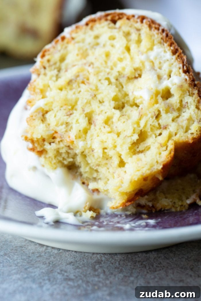 The Ultimate Banana Bundt 9 A slice of banana bundt cake with white creamy frosting on a blue plate.