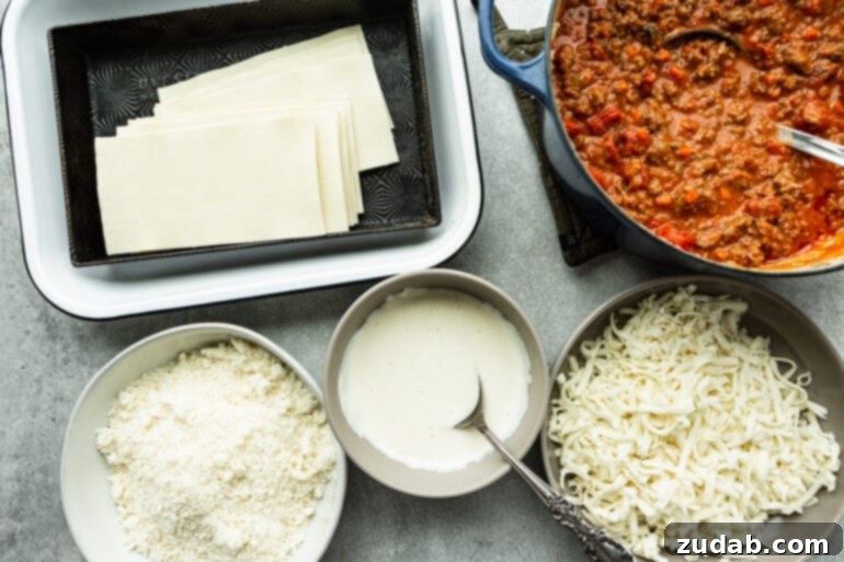 My Go-To Lasagna Masterpiece 4 A vibrant flat lay photo displays all the fresh and prepared ingredients for homemade lasagna, including uncooked lasagna noodles, a bowl of rich meaty tomato bolognese sauce, a separate bowl of shredded mozzarella cheese, a creamy white béchamel sauce, and grated Parmesan cheese, ready for assembly.