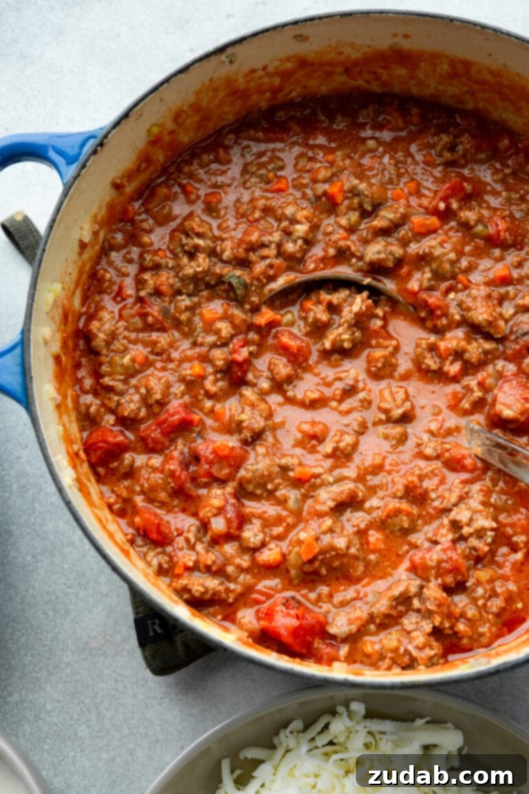 My Go-To Lasagna Masterpiece 6 A large, rustic Dutch oven filled to the brim with rich, meaty tomato bolognese sauce, simmering gently on a stovetop, ready to be incorporated into the lasagna.
