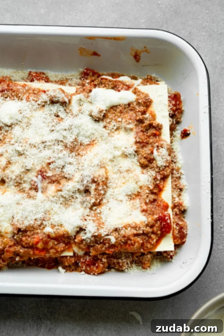 My Go-To Lasagna Masterpiece 8 A captivating view of a lasagna in mid-assembly within a baking dish, showcasing perfect layers of rich meat sauce, flat pasta noodles, and generous amounts of shredded cheese, ready for the next step.