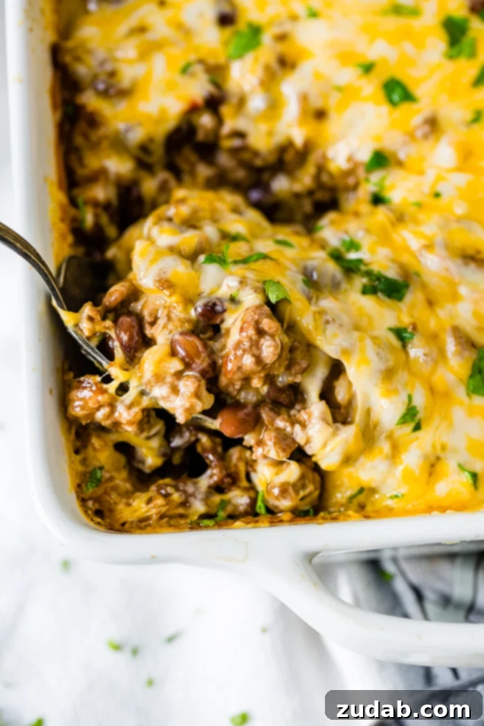 Zesty Beef and Rice Cheese Bake 2 A white casserole dish filled with Cheesy Mexican Ground Beef and Rice Casserole, with a large spoon scooping out a portion.
