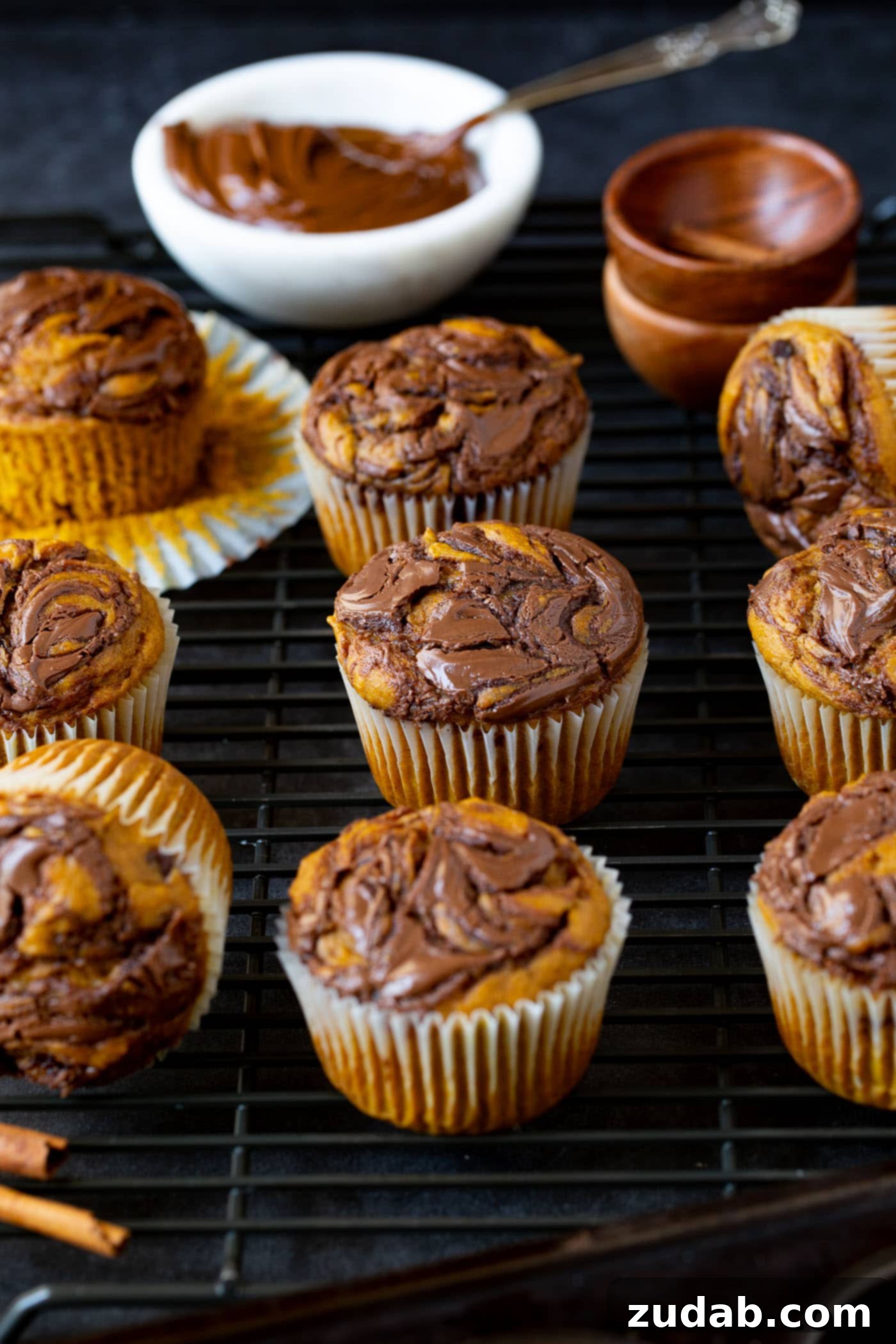 Nutella Swirled Pumpkin Muffins Ten Nutella swirled pumpkin muffins. The paper liner has been peeled back on one of the muffins, and a small bowl of Nutella is in the background.