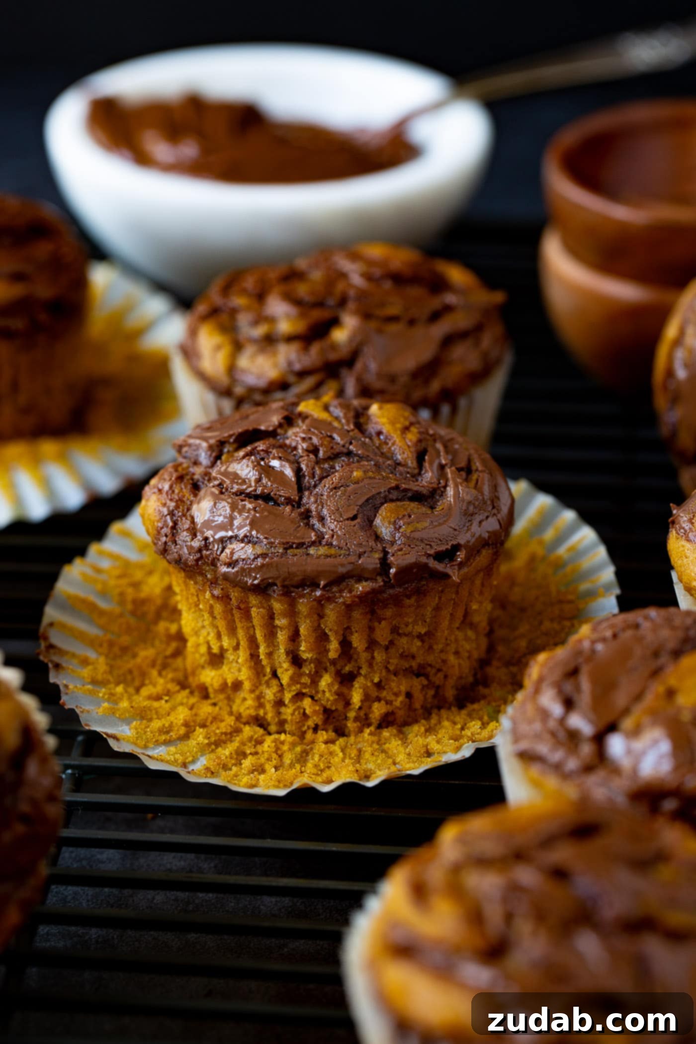 Nutella Swirled Pumpkin Muffins Nutella swirled pumpkin muffins. The paper muffin liners are peeled back so you can see the soft pumpkin muffin with the nutella swirled through it.