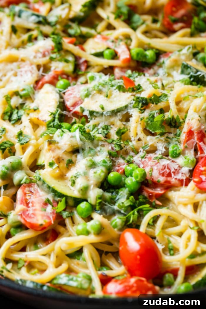 Kicking Queso Spring Pasta 2 A vibrant skillet of spaghetti pasta, zucchini, peas, and tomatoes generously coated in a luscious spicy queso sauce, promising a delightful fusion of flavors.