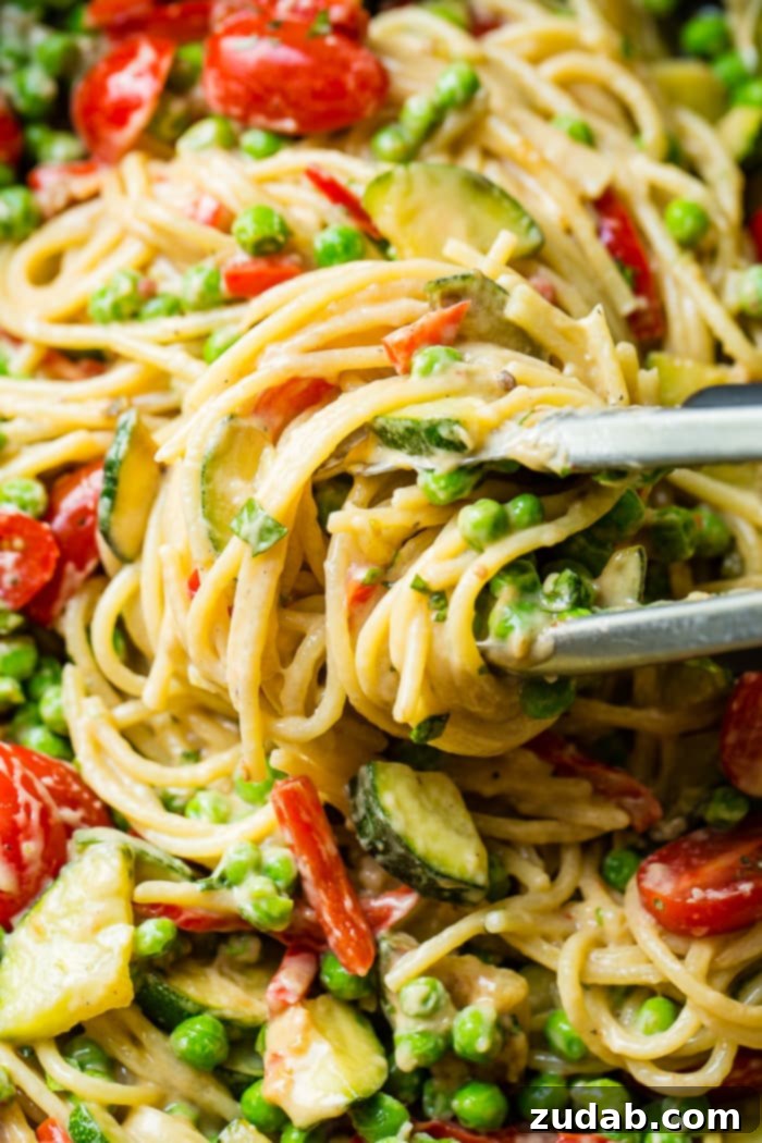 Kicking Queso Spring Pasta 4 A close-up shot of the Spicy Queso Pasta Primavera in a large skillet, showing the perfectly cooked spaghetti, tender zucchini, vibrant peas, and juicy tomatoes bathed in a rich, mild queso sauce, garnished with fresh cilantro.