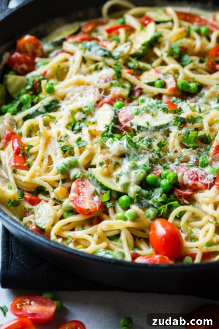 Kicking Queso Spring Pasta 5 A generously filled large skillet showcasing Spicy Queso Pasta Primavera, featuring golden spaghetti, colorful zucchini, peas, and tomatoes bathed in a rich, creamy sauce.