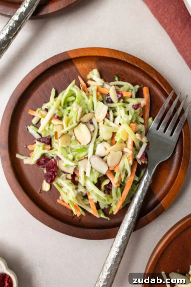 A serving of homemade broccoli slaw presented on a small wooden plate, with a fork resting beside it, highlighting its fresh and inviting texture.