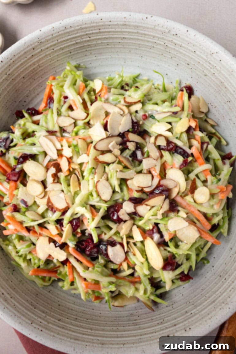 A large serving bowl filled with a generous portion of broccoli slaw, mixed with sweet craisins and crunchy sliced almonds, ready for a gathering.