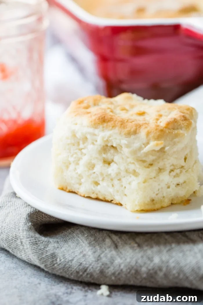 Surprisingly Easy 7 Up Biscuits 7 a gray napkin with a white plate, cut open 7 Up and bisquick biscuit with strawberry jam and a jar of ham and pan of biscuits behind it