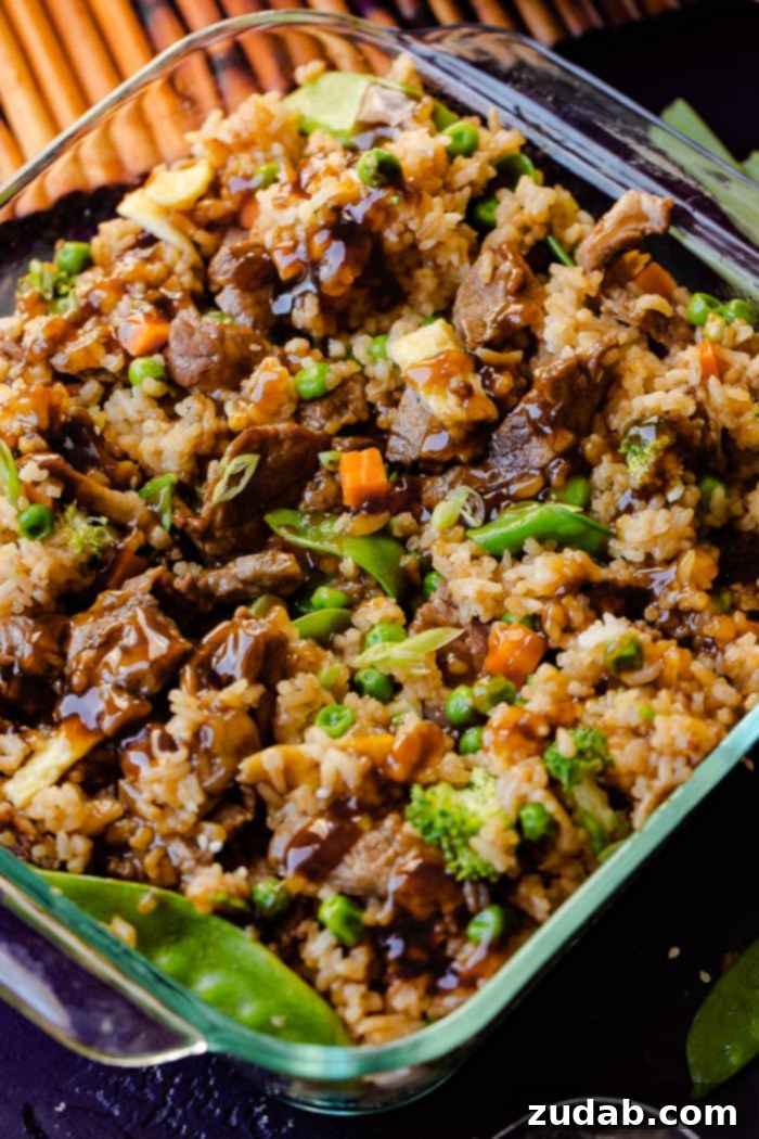 Teriyaki Beef Bake 5 a glass casserole dish with fried rice, carrots, peas, broccoli, snow peas, and teriyaki beef