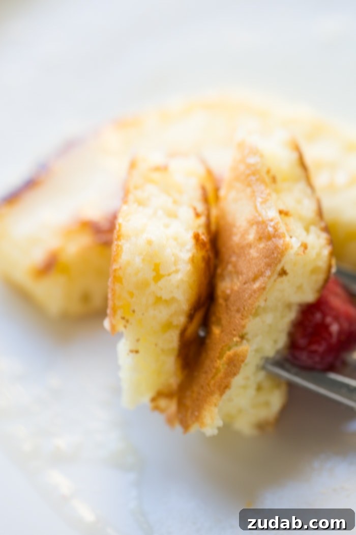 Cloud-Like Sour Cream Pancakes 5 a couple of pieces of cut melt in your mouth sour cream pancakes on a fork with a small raspberry