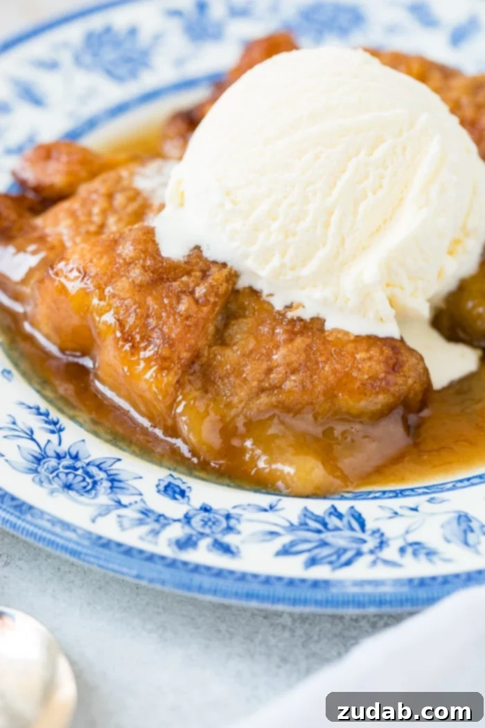 Sparkling Sprite Apple Dumplings 2 Two golden-brown apple dumplings drizzled with caramel sauce and topped with vanilla ice cream, served on a blue china plate.