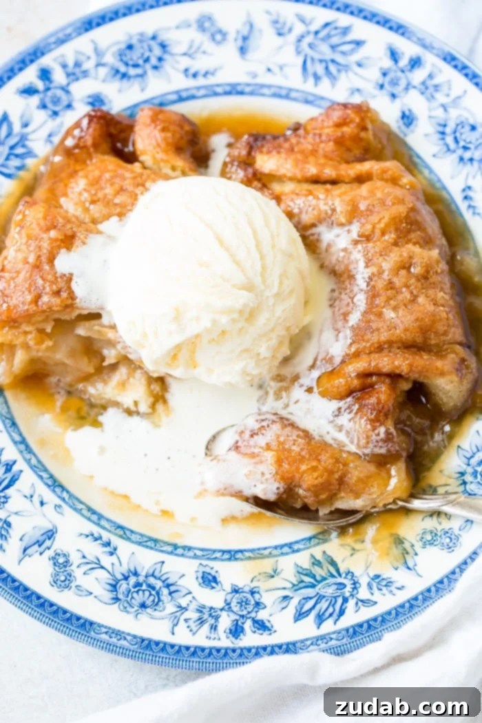 Sparkling Sprite Apple Dumplings 3 A close-up of two warm apple dumplings with melted caramel sauce and a scoop of vanilla ice cream, on a elegant blue china plate.