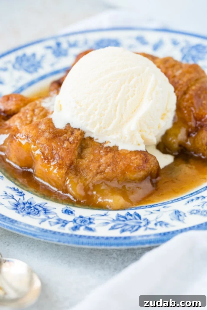Sparkling Sprite Apple Dumplings 7 A close-up of a single apple dumpling, rich with caramel sauce and melting vanilla ice cream, on a blue china plate.