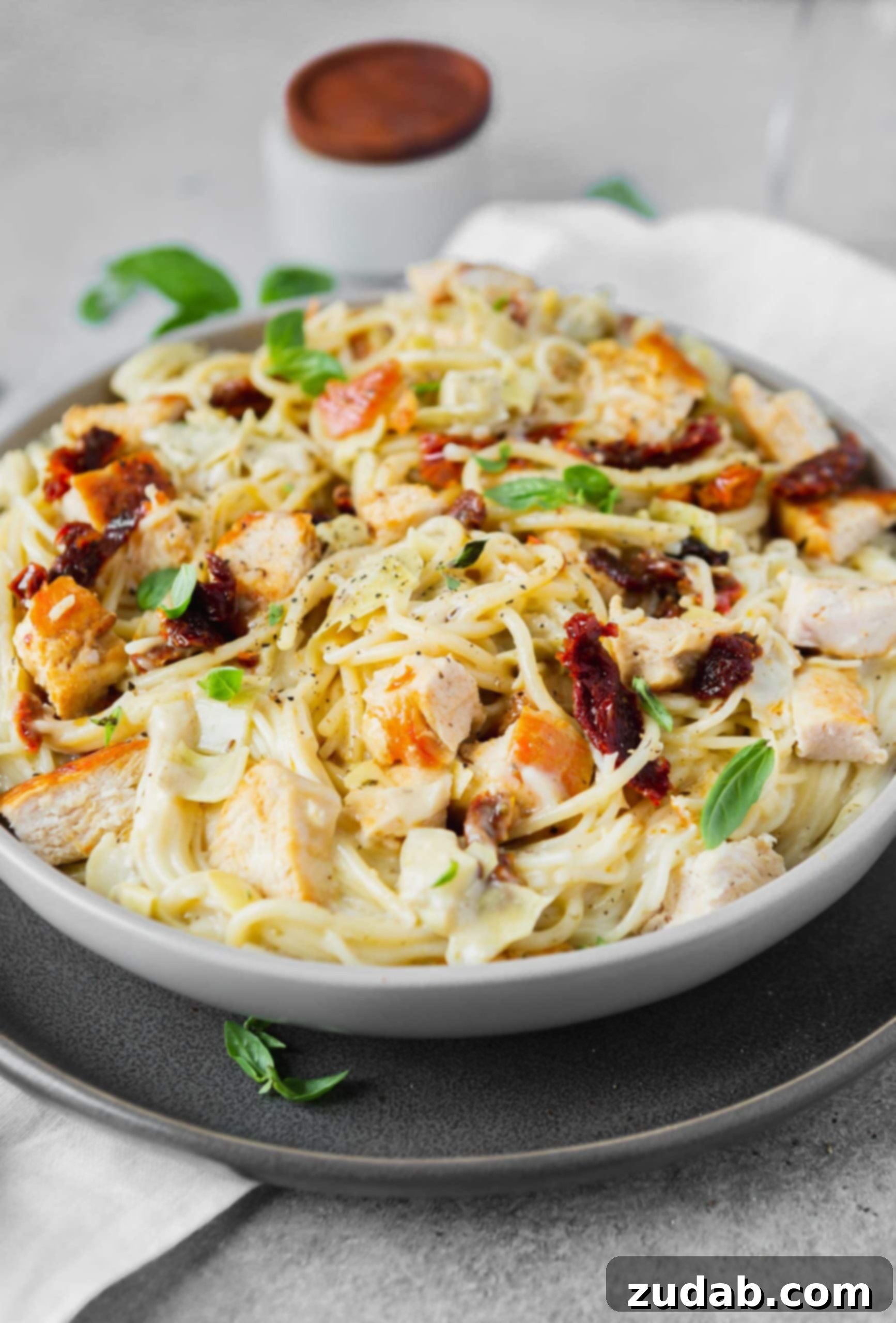 Creamy Chicken Artichoke Pasta a photo of creamy chicken artichoke pasta in a large bowl topped with large chunks of golden chicken breasts.