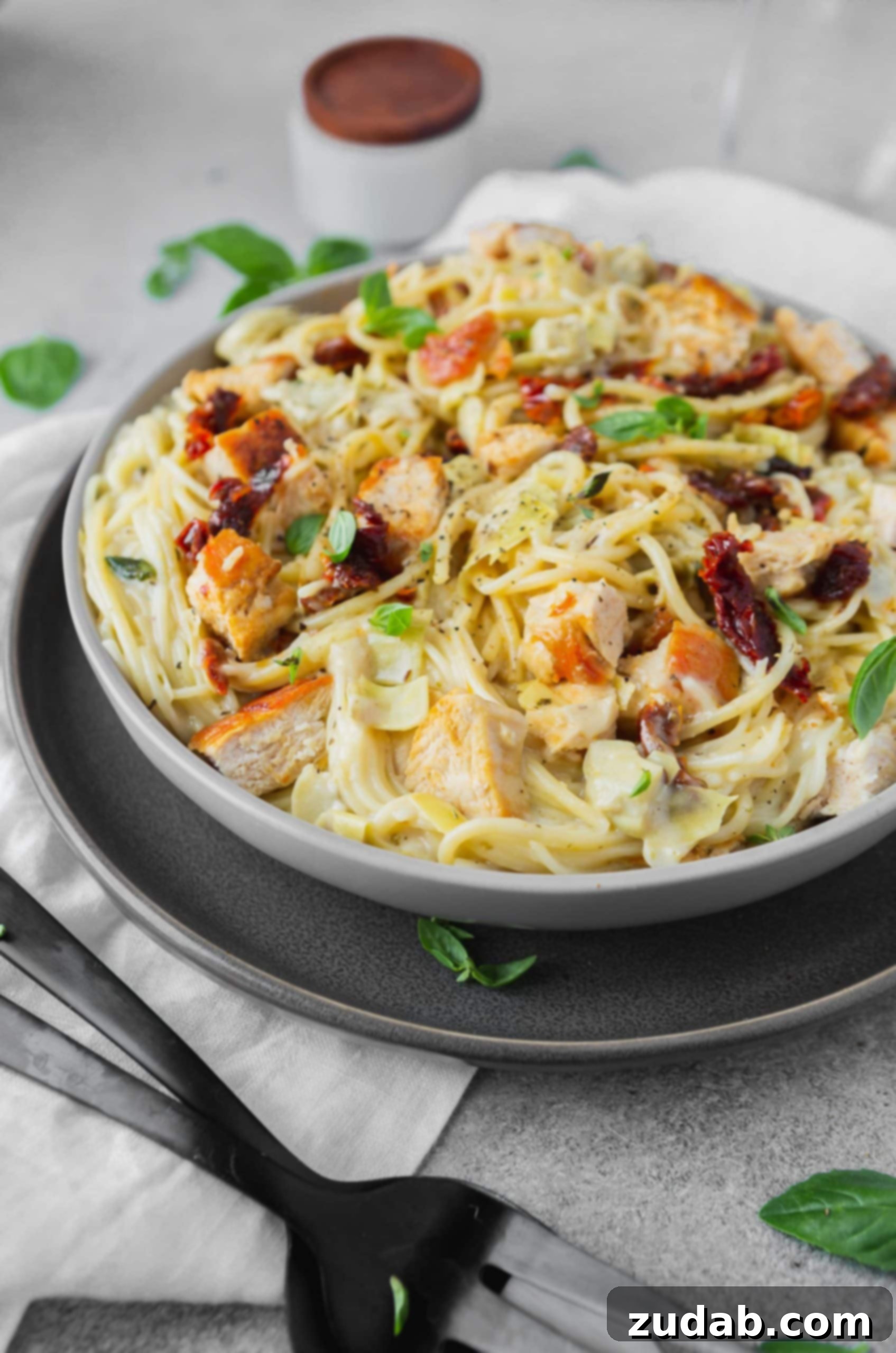 Creamy Chicken Artichoke Pasta a photo of creamy chicken pasta with sun dried tomatoes and fresh basil on top.