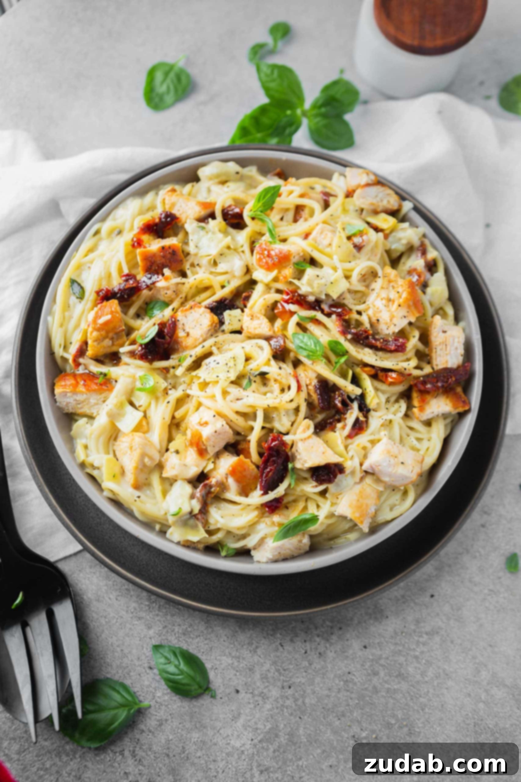 Creamy Chicken Artichoke Pasta a photo of creamy chicken pasta with sun dried tomatoes and fresh basil on top.
