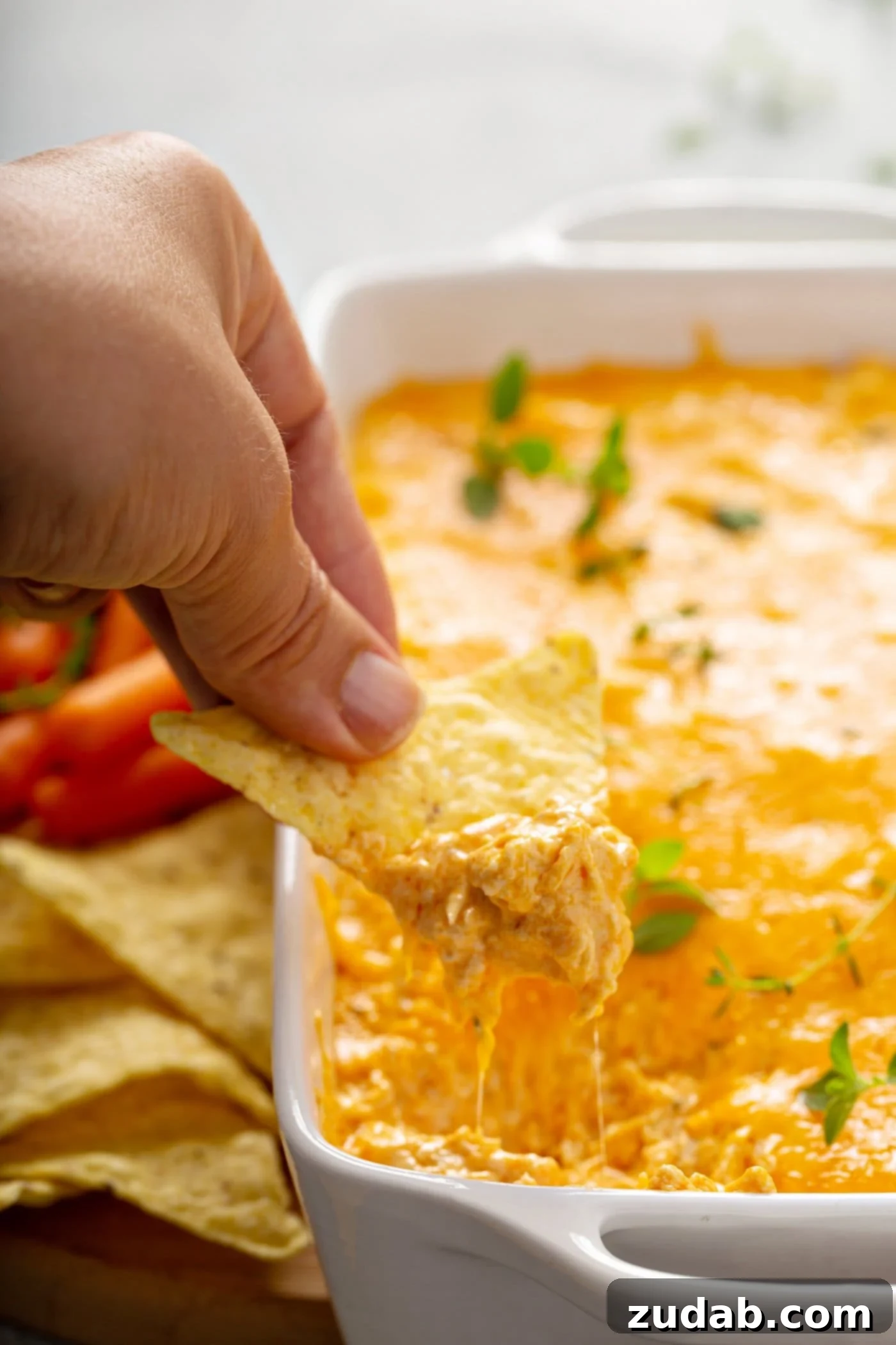 Instant Pot Buffalo Chicken Dip A chip is being dipped into buffalo chicken dip. There is other chips and carrot sticks in the background.