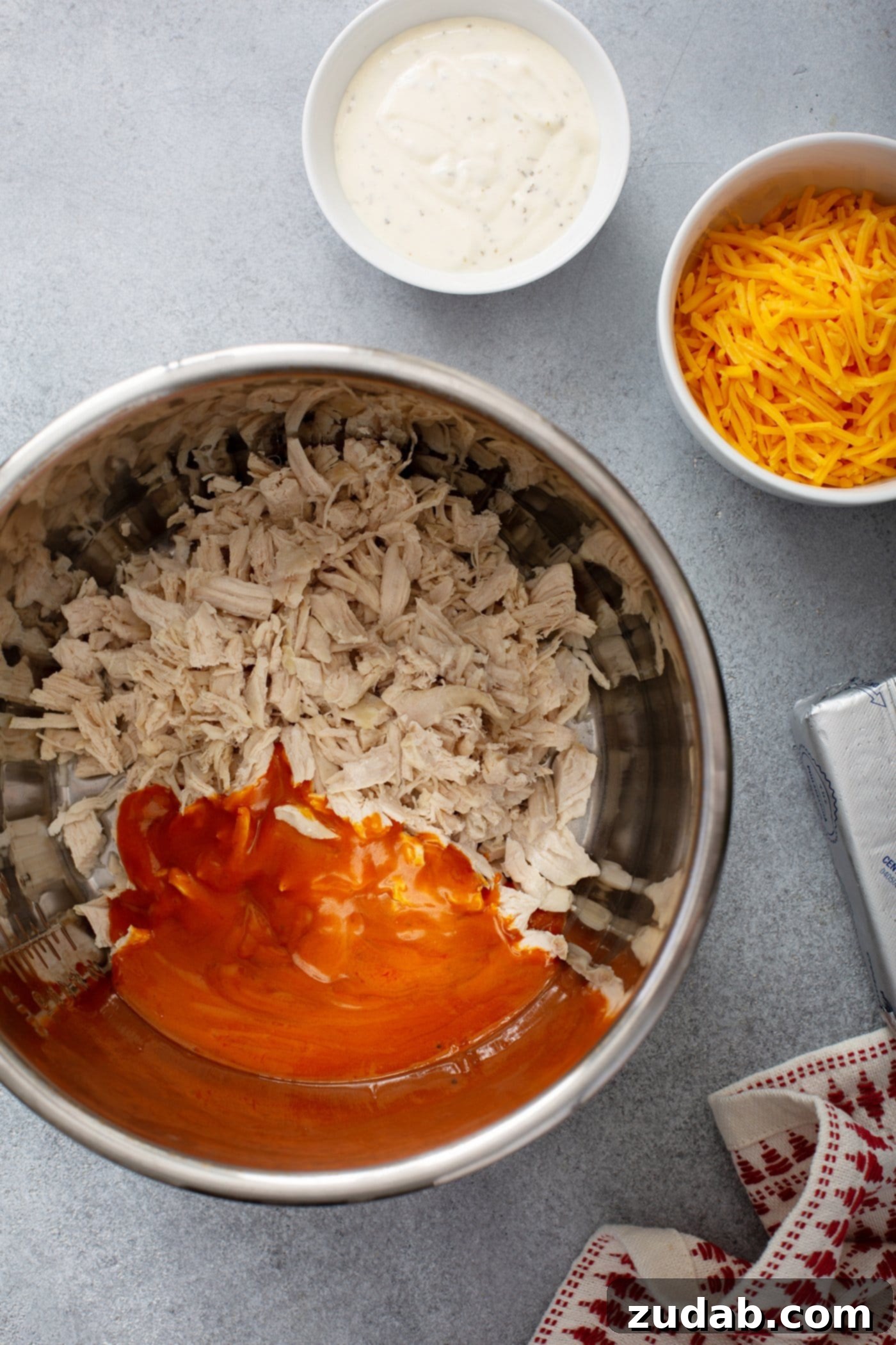 Instant Pot Buffalo Chicken Dip An instant pot with shredded chicken and buffalo sauce. Small bowls of ranch dressing and shredded cheese are in the background.
