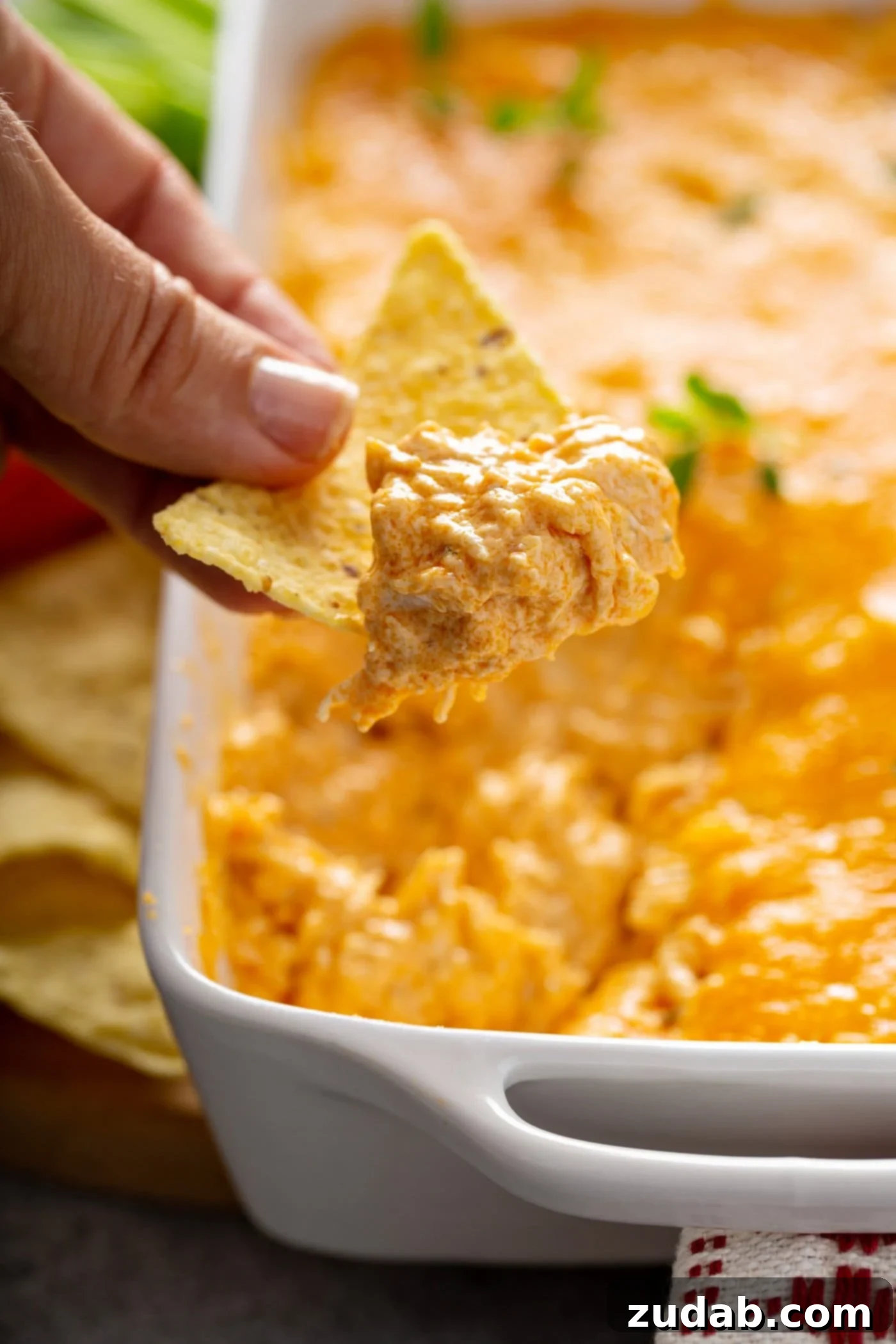 Instant Pot Buffalo Chicken Dip A chip that has been dipped in buffalo chicken dip. There is shredded chicken and melted cheese on the chip. More chips are in the background.