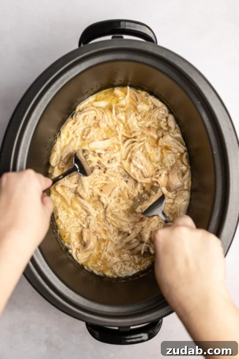 Set It and Forget It Chicken and Rice 3 Creamy meat mixture in a crockpot with forks pulling the meat.