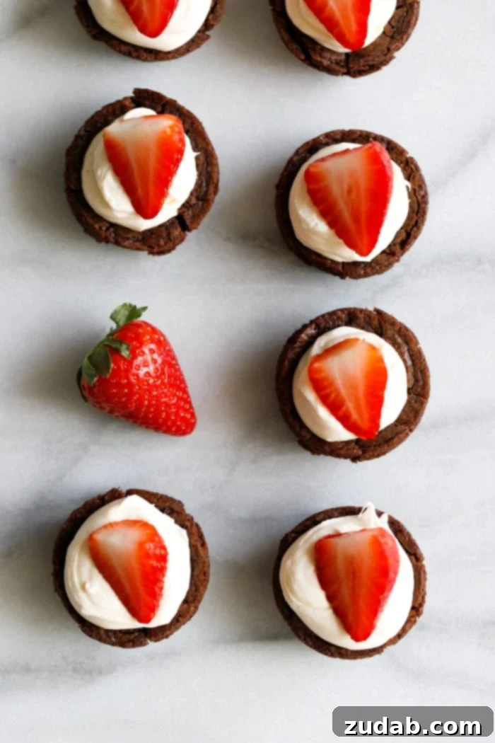 Black Tie Brownie Treats 3 A marble background with tiny brownie cups filled with a white chocolate cream cheese filling and a sliced strawberry on top making these the cutest tuxedo brownie cups