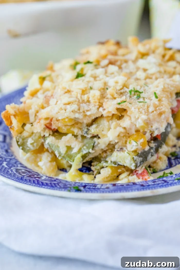 Golden Zucchini Corn Gratin 2 A golden-brown slice of cheesy zucchini corn casserole on a blue china plate, showcasing layers of zucchini, corn, peppers, melted cheese, and a crunchy buttered cracker topping.