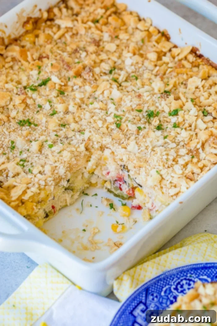 Golden Zucchini Corn Gratin 3 A full white casserole dish of layered cheesy zucchini corn casserole, with one slice removed, revealing the vibrant layers of grilled zucchini, sweet corn, bell peppers, and rich melted cheese under a golden-brown cracker topping.