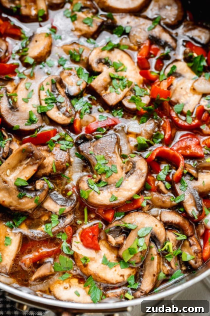 Delicious Italian Sauteed Mushrooms 2 A close-up photo of perfectly sautéed Italian mushrooms with vibrant sliced red peppers and onions, generously topped with fresh chopped parsley, glistening with a savory sauce.