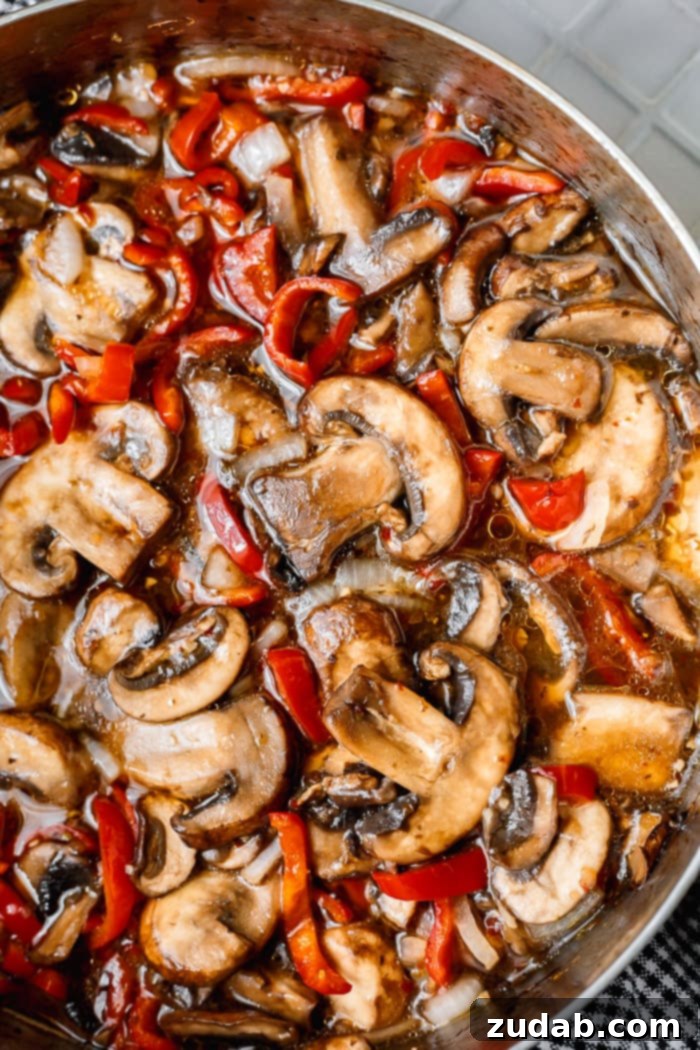 Delicious Italian Sauteed Mushrooms 5 A photo of saucy sauteed baby bella mushrooms with sliced red bell peppers and onions simmering in a saute pan, ready to be served.
