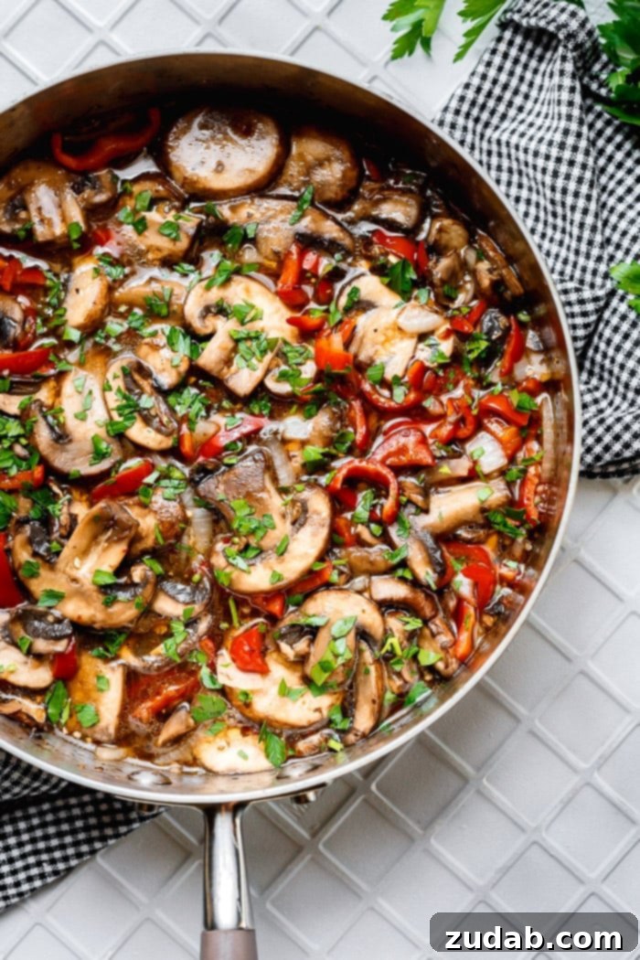 Delicious Italian Sauteed Mushrooms 6 A deep saute pan filled with perfectly sliced and saucy sautéed mushrooms, vibrant red bell peppers, and diced onions, all generously topped with freshly chopped parsley for garnish.