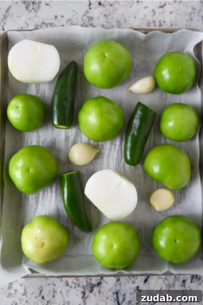 Roasted tomatillos, jalapeños, and onions on a baking sheet, essential for the enchilada sauce.