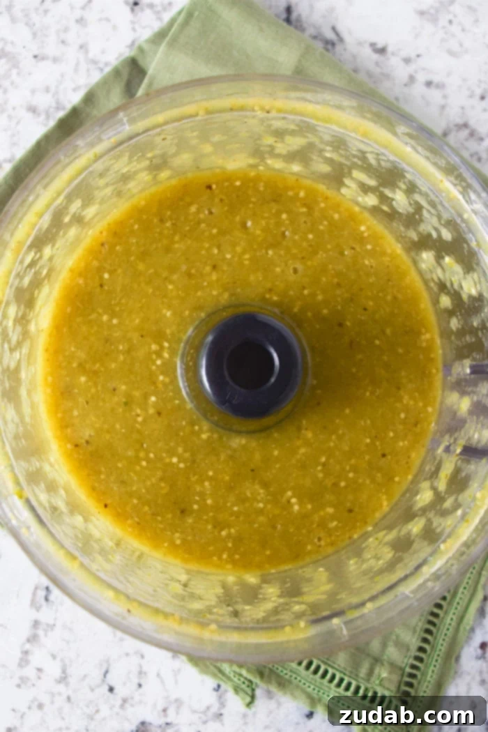 Rich and creamy roasted tomatillo sauce simmering in a skillet, ready for enchilada assembly.