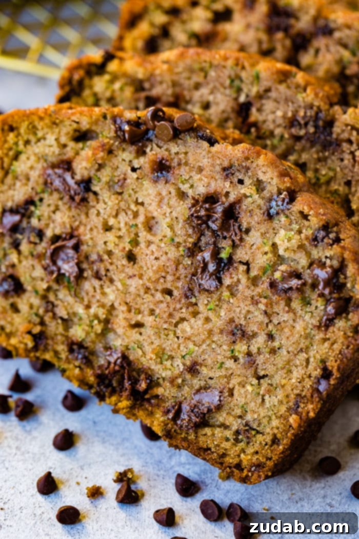 Decadent Chocolate Chip Zucchini Bread 2 a photo of a slice of chocolate chip zucchini bread with two more slices stacked behind it that are full of mini chocolate chips all sitting on the counter with mini chocolate chips sprinkled on the counter in front of the bead