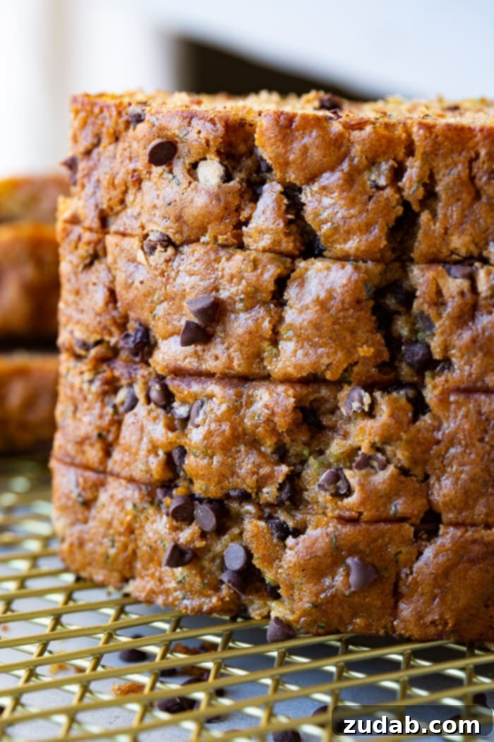 Decadent Chocolate Chip Zucchini Bread 3 a photo of a stack of four slices of homemade zucchini bread sitting on a gold wire cooling rack with the slices laying on their side looking at the top of the bread which is sprinkled with mini chocolate chips