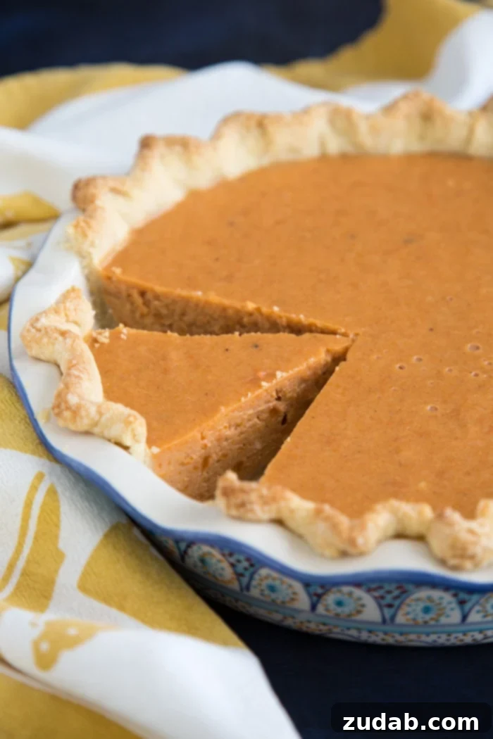 Sweet Potato Pie, made with cream cheese in the filling, a cross between a pie and a cheesecake, guaranteed to be a hit for the holidays. #sweetpotato #sweetpotatopie #sweetpotatocheesecake #holidays A whole Sweet Potato Pie, featuring a rich, creamy filling infused with cream cheese, beautifully set in a golden, flaky crust, resting on a cooling rack. This dessert is a perfect blend of pie and cheesecake, ideal for any holiday celebration.