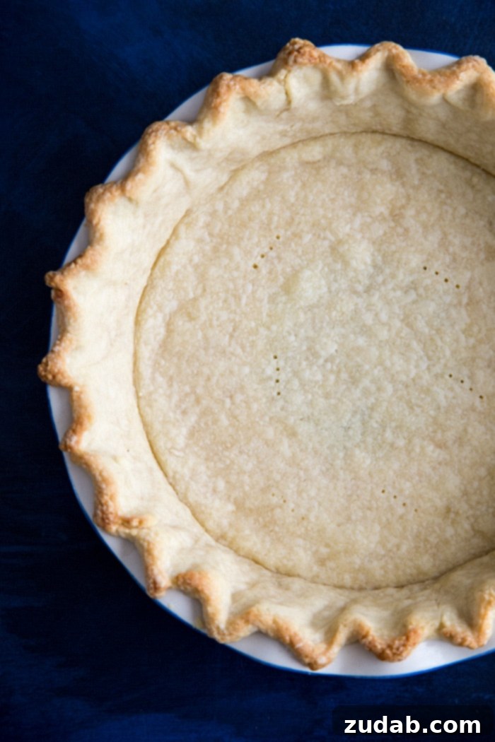 Par-baked pie crust for Sweet Potato Pie A beautifully golden-brown, par-baked pie crust with elegantly crimped edges, sitting on a wire rack, perfectly prepared and ready to be filled with the creamy sweet potato and cheesecake filling for a homemade holiday pie.