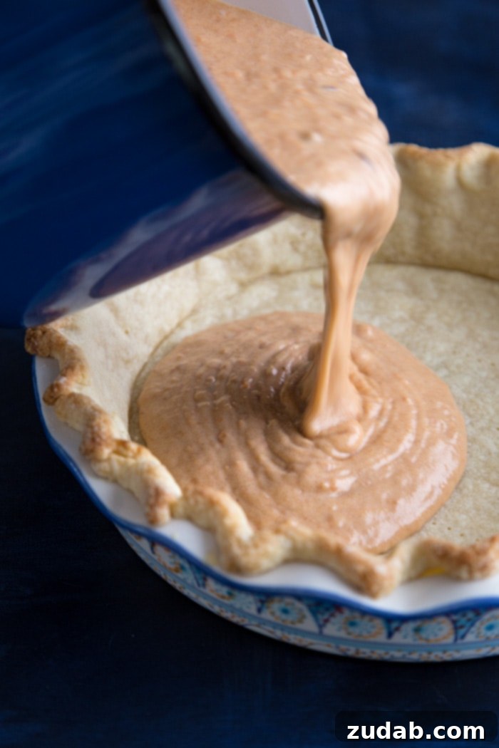 Pouring Sweet Potato Pie filling into pie crust Rich, creamy sweet potato cheesecake filling, smooth and vibrant, being carefully poured into a golden, par-baked pie crust. This crucial step prepares the dessert for its final bake, creating a perfect holiday treat.
