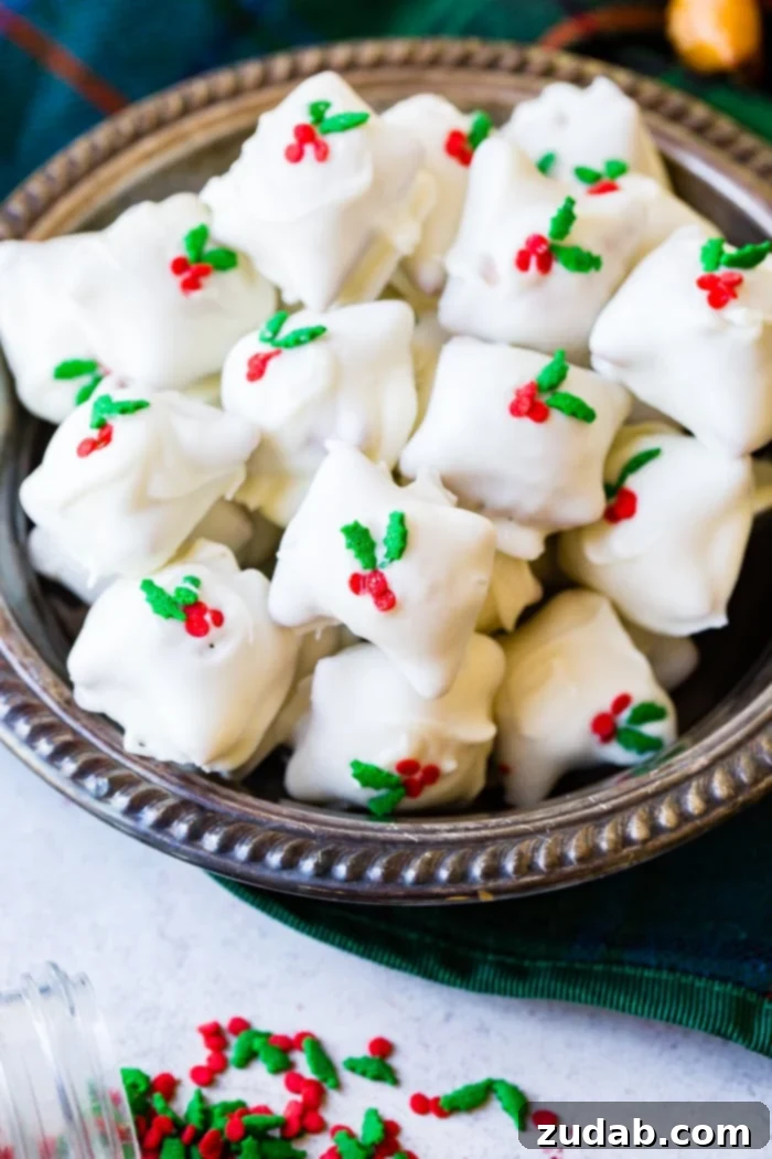 Holiday Peanut Butter White Chocolate Pretzel Crunch 2 A silver bowl brimming with white chocolate-dipped peanut butter-filled pretzels, adorned with vibrant holly berry sprinkles, ready for Christmas celebrations.