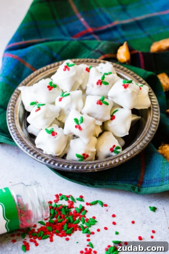 Holiday Peanut Butter White Chocolate Pretzel Crunch 3 A glistening silver bowl overflowing with white chocolate-covered peanut butter pretzels, sprinkled with cheerful holly berries, a perfect holiday dessert.