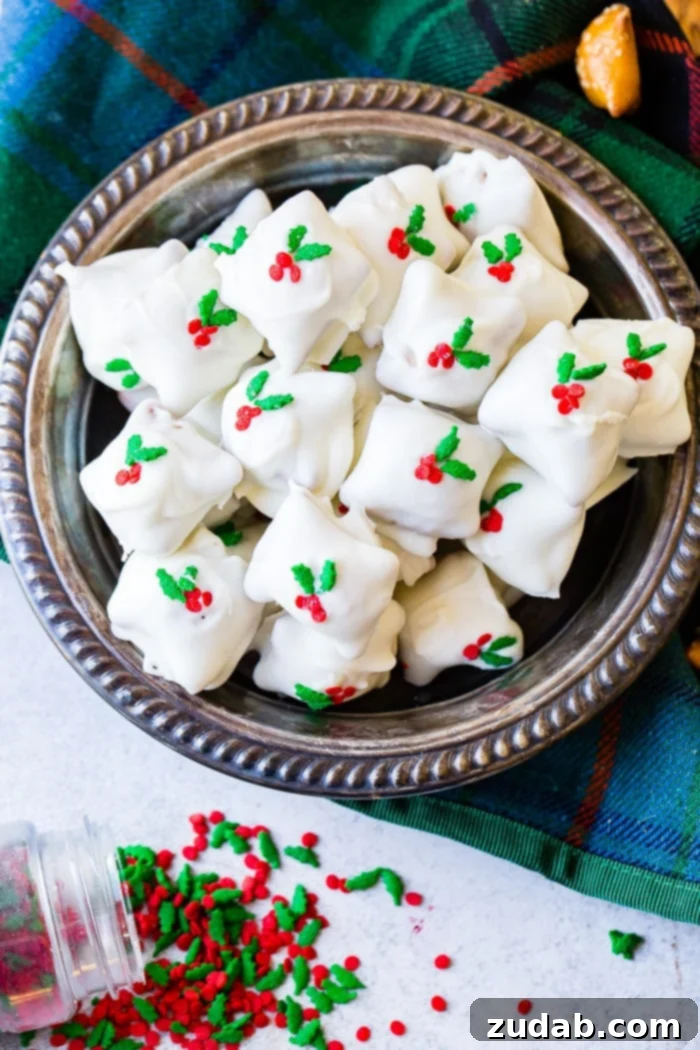 Holiday Peanut Butter White Chocolate Pretzel Crunch 5 A festive silver bowl brimming with white chocolate-covered peanut butter pretzels, generously sprinkled with holly berry decorations, a delightful holiday dessert.