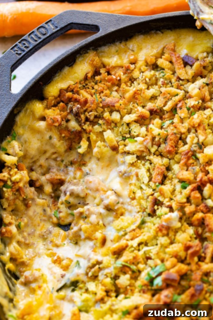 Hearty Creamy Zucchini Sausage Bake 3 A close-up view of a creamy zucchini sausage casserole, richly topped with golden stuffing, presented in a cast iron skillet with a scoop already taken out, revealing the delicious layers beneath.