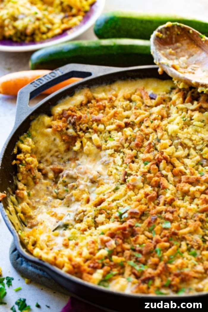 Hearty Creamy Zucchini Sausage Bake 7 A serving of creamy zucchini sausage casserole, topped with golden-brown stuffing, nestled in a cast iron skillet with a portion removed, showcasing its delicious texture.