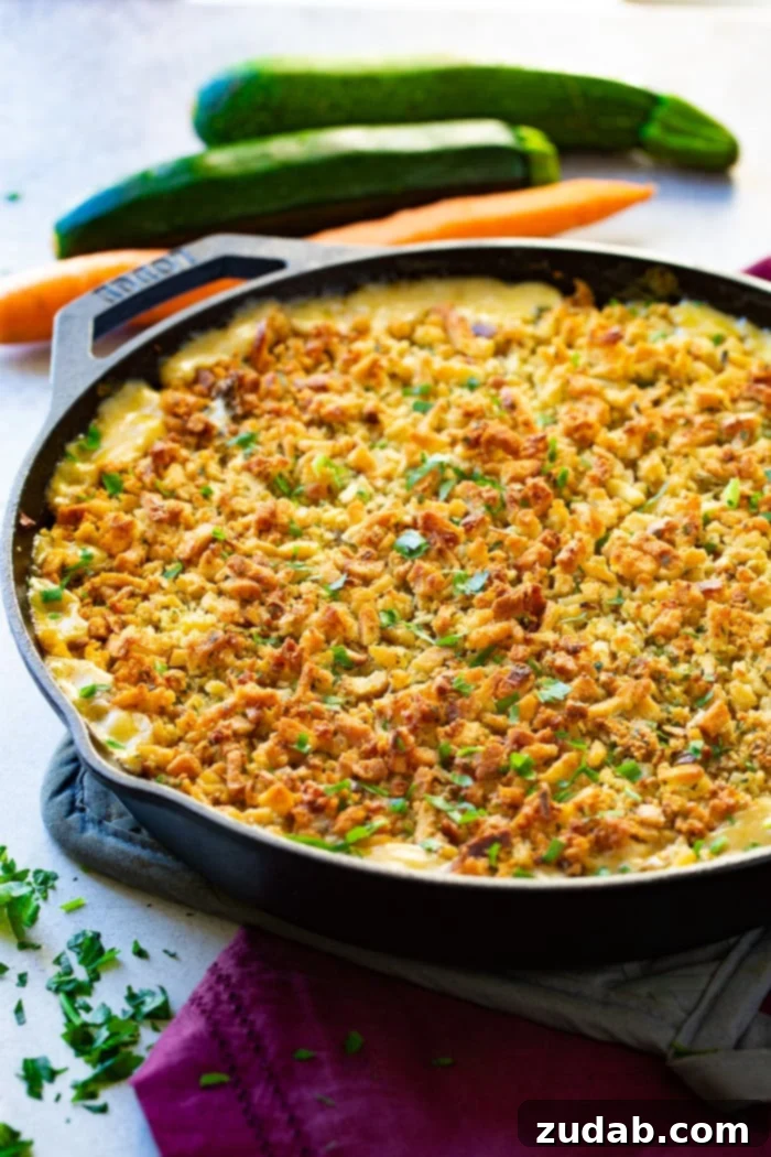 Hearty Creamy Zucchini Sausage Bake 8 A cast iron skillet holds a creamy casserole, beautifully crowned with a toasty golden stuffing topping, resting on a pot holder with a fresh carrot in the background, showcasing its comforting appeal.
