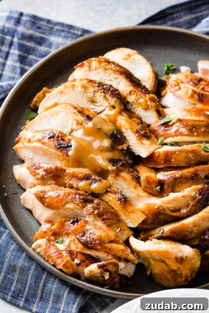 A dark grey plate with perfectly sliced apple pecan smoked turkey breast, garnished with fresh thyme leaves, ready for serving.