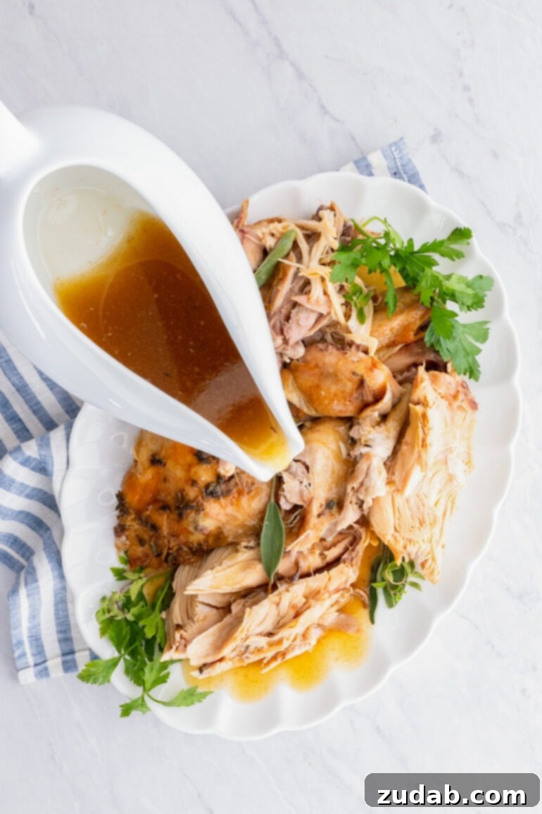 A gleaming gravy boat, overflowing with rich, homemade gravy, sits invitingly atop a platter generously piled with tender, juicy chunks of turkey, ready to be enjoyed.