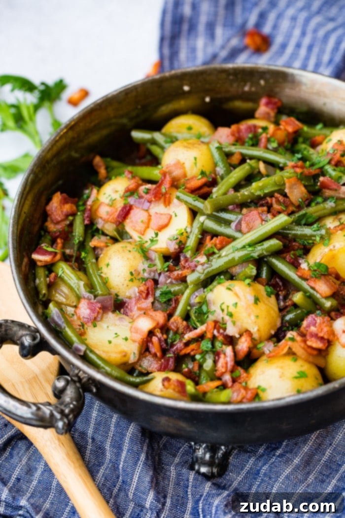 Effortless Instant Pot Green Beans and Potatoes 5 a photo of a large silver serving dish full of cookie green beans, halved potatoes and chopped parsley and crispy pieces of bacon