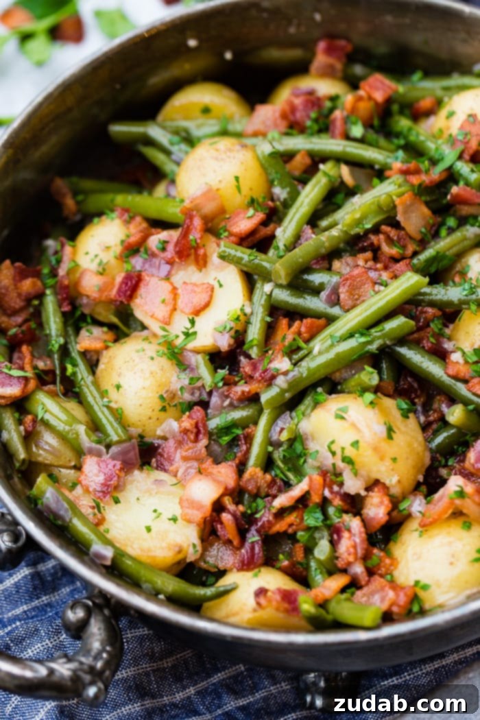 Effortless Instant Pot Green Beans and Potatoes 7 A photo of a silver serving dish sitting on a blue cloth napkin that is full of cooked fresh green beans, potatoes, and bacon pieces sprinkled with fresh parsley.